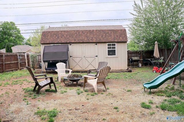 view of yard with an outdoor fire pit, a shed, a fenced backyard, an outbuilding, and a playground