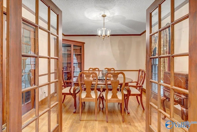 dining space featuring a textured ceiling, a notable chandelier, ornamental molding, and light hardwood / wood-style flooring