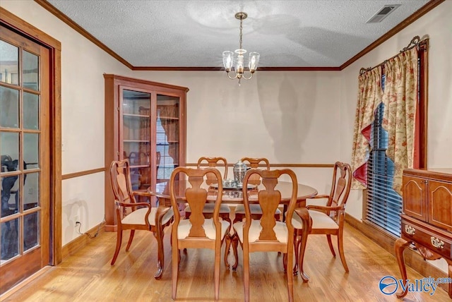 dining room with a chandelier, a textured ceiling, crown molding, and light hardwood / wood-style flooring