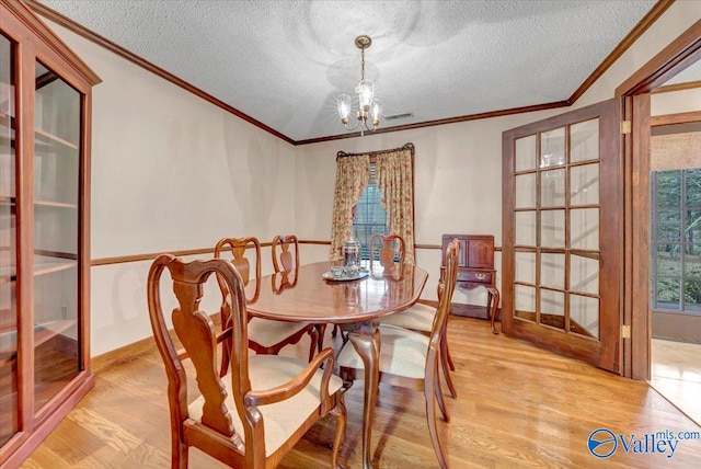 dining area featuring a textured ceiling, light hardwood / wood-style flooring, crown molding, and a notable chandelier