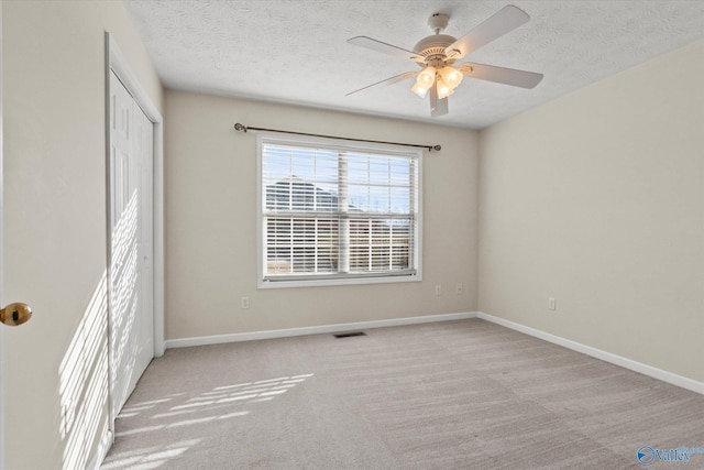 spare room featuring light colored carpet, ceiling fan, and a textured ceiling