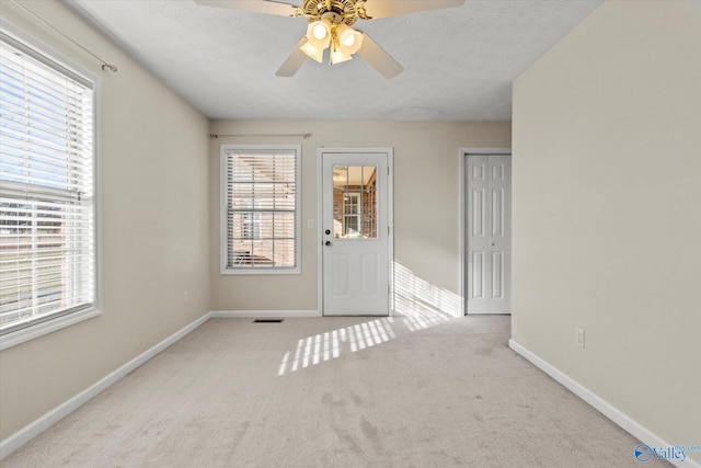 empty room featuring ceiling fan, light carpet, and a textured ceiling