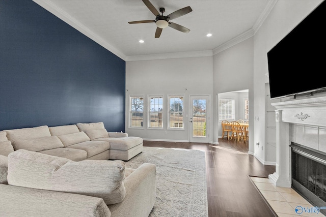 living room with light wood-type flooring, ceiling fan, ornamental molding, a fireplace, and a high ceiling