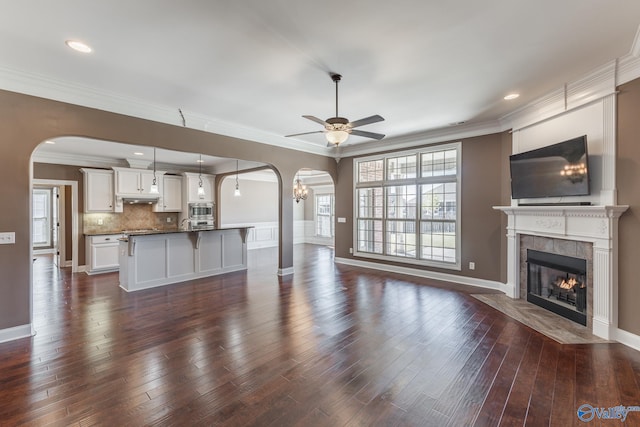 unfurnished living room featuring crown molding, dark hardwood / wood-style floors, a tile fireplace, and ceiling fan