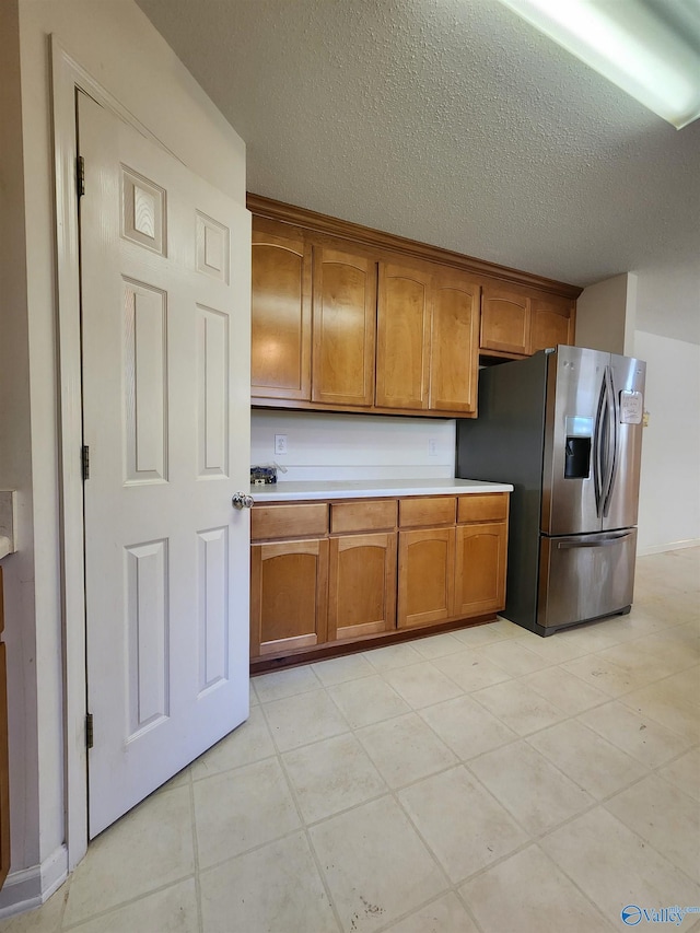 kitchen with stainless steel fridge, light tile patterned floors, and a textured ceiling