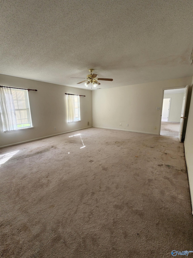 carpeted empty room featuring ceiling fan, plenty of natural light, and a textured ceiling