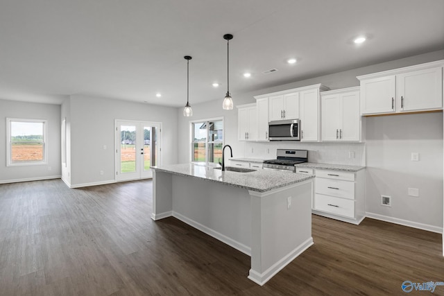 kitchen featuring light stone countertops, hanging light fixtures, a kitchen island with sink, white cabinetry, and appliances with stainless steel finishes