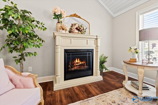 living area with a warm lit fireplace, baseboards, wood finished floors, and vaulted ceiling