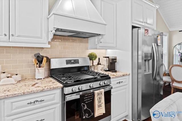 kitchen featuring appliances with stainless steel finishes, premium range hood, white cabinetry, vaulted ceiling, and decorative backsplash