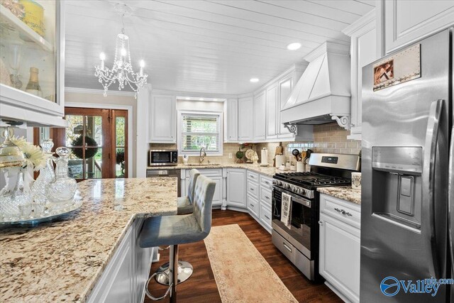 kitchen featuring custom exhaust hood, a notable chandelier, white cabinetry, crown molding, and appliances with stainless steel finishes