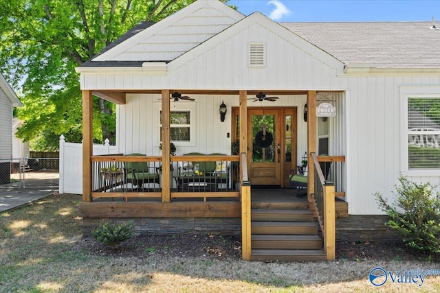 view of exterior entry with a ceiling fan, fence, a shingled roof, and board and batten siding