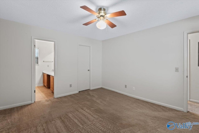 unfurnished bedroom featuring connected bathroom, light colored carpet, a textured ceiling, and ceiling fan