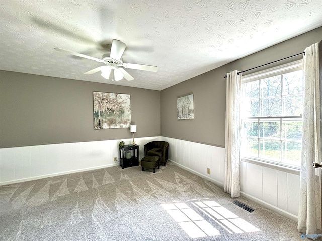 unfurnished room with a wainscoted wall, carpet flooring, a textured ceiling, visible vents, and ceiling fan