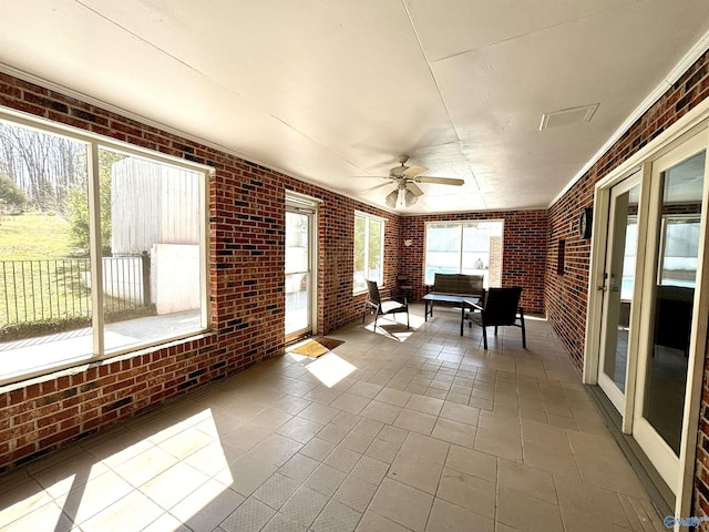 unfurnished sunroom featuring ceiling fan and brick wall