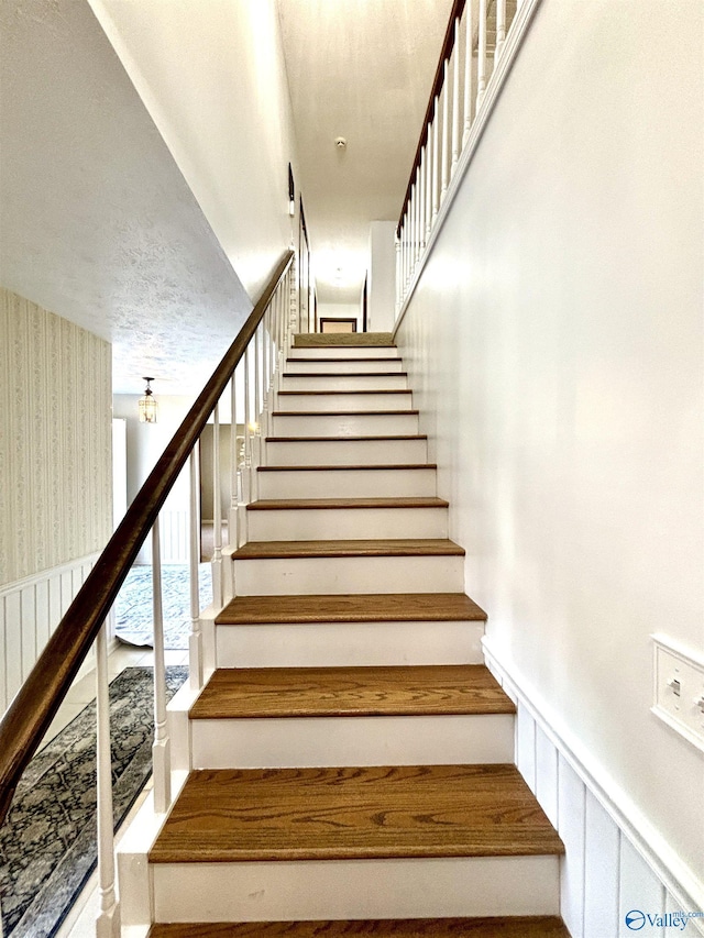 stairway featuring wallpapered walls and wainscoting