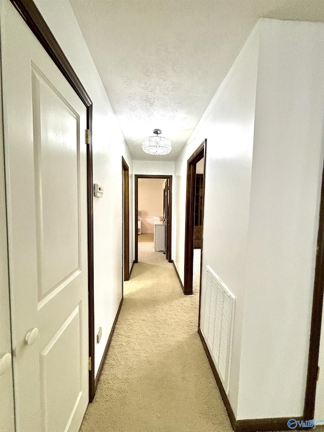 hallway featuring light colored carpet, visible vents, baseboards, and a textured ceiling