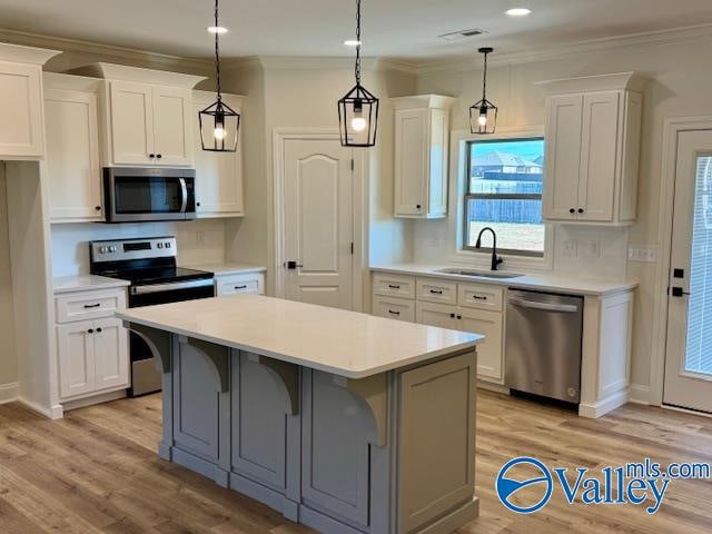 kitchen with appliances with stainless steel finishes, white cabinetry, a kitchen island, and light hardwood / wood-style flooring