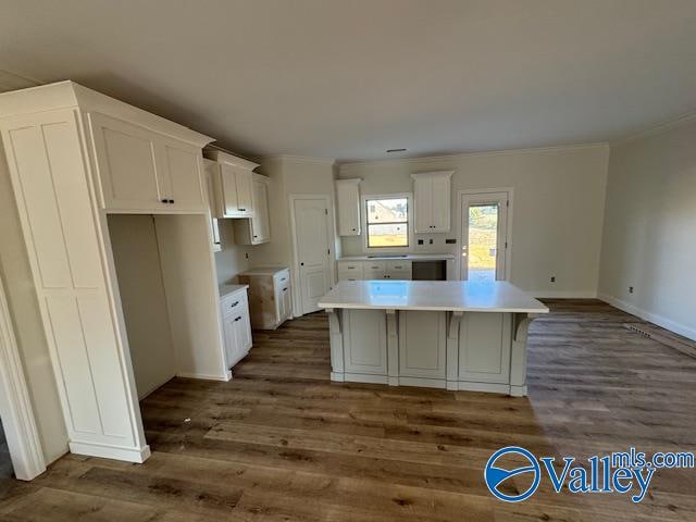 kitchen with white cabinets, ornamental molding, a center island, and dark wood-type flooring