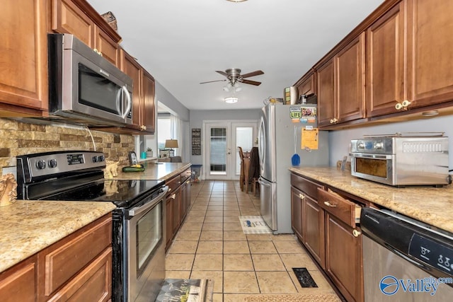 kitchen with light stone counters, ceiling fan, stainless steel appliances, and light tile patterned floors