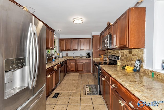 kitchen with appliances with stainless steel finishes, sink, decorative backsplash, light tile patterned floors, and light stone countertops