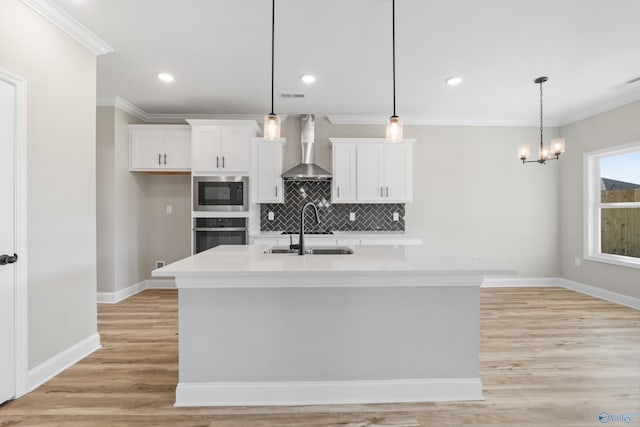 kitchen with white cabinets, a kitchen island with sink, sink, and wall chimney range hood