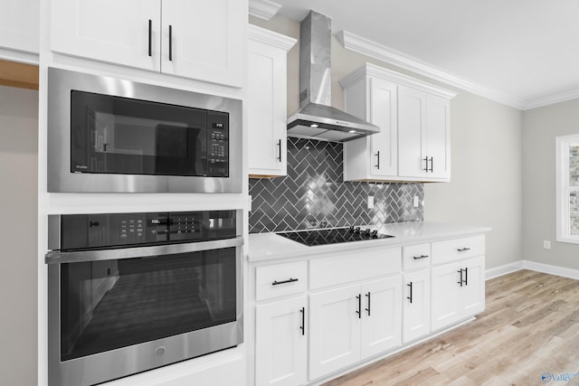 kitchen with built in microwave, wall chimney exhaust hood, white cabinetry, black electric stovetop, and oven