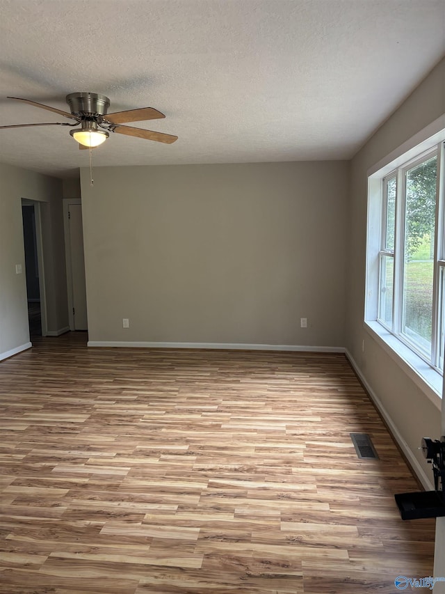 empty room with ceiling fan, a textured ceiling, light wood-style flooring, baseboards, and visible vents