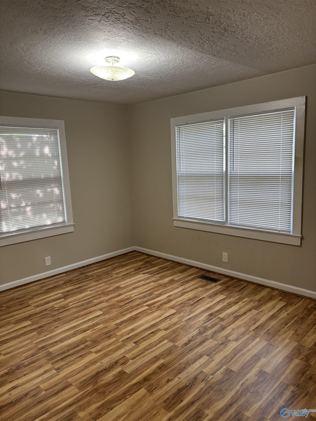 unfurnished room featuring baseboards, a textured ceiling, and wood finished floors