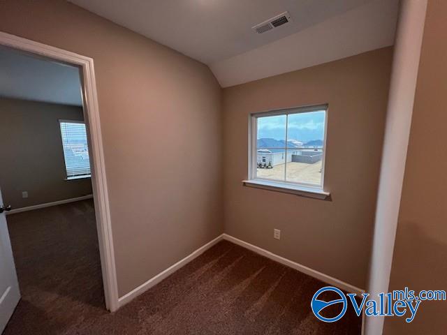 empty room featuring vaulted ceiling and dark colored carpet