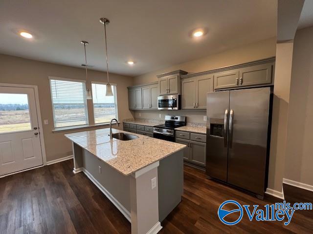 kitchen featuring light stone countertops, stainless steel appliances, dark wood-type flooring, sink, and hanging light fixtures