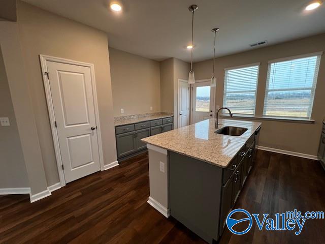 kitchen with a center island with sink, sink, dark hardwood / wood-style floors, light stone countertops, and decorative light fixtures