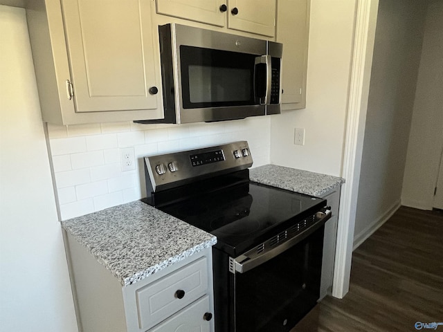 kitchen featuring light stone countertops, backsplash, appliances with stainless steel finishes, and dark wood-style floors