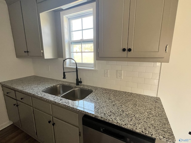 kitchen with dishwasher, light stone counters, decorative backsplash, gray cabinets, and a sink