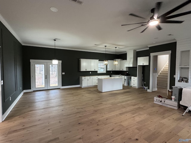 kitchen featuring pendant lighting, crown molding, white cabinets, a kitchen island, and wall chimney exhaust hood