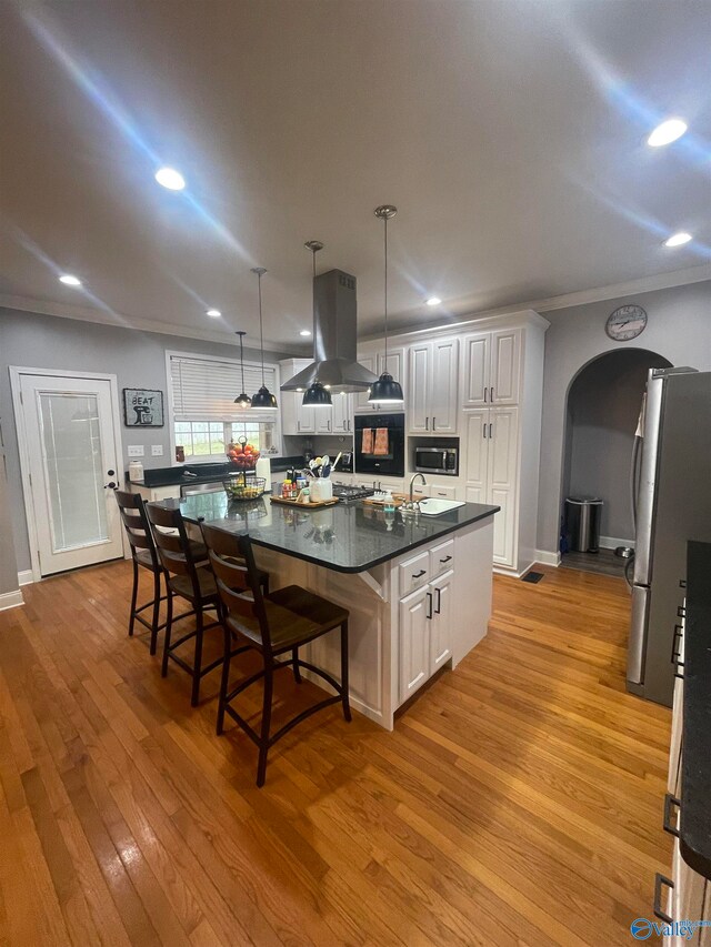 kitchen with hanging light fixtures, appliances with stainless steel finishes, a large island with sink, white cabinetry, and island exhaust hood