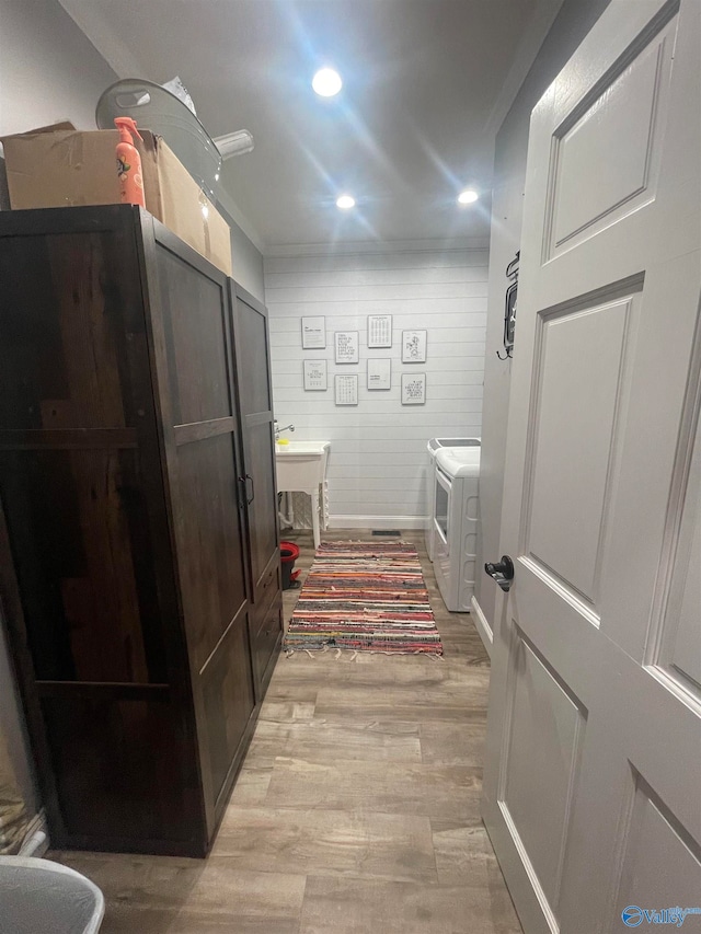 bathroom with hardwood / wood-style floors, wooden walls, washing machine and clothes dryer, and ornamental molding