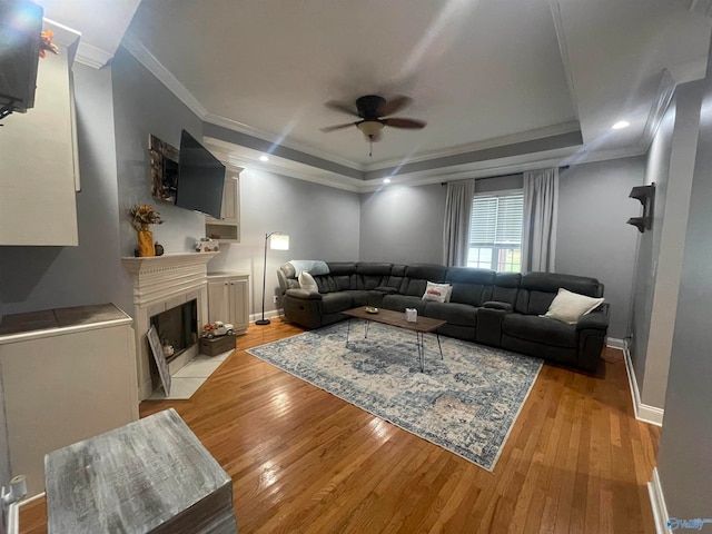 living room featuring a raised ceiling, ceiling fan, ornamental molding, and light hardwood / wood-style floors