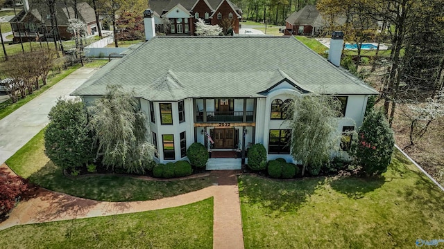 tudor house with roof with shingles, a front yard, stucco siding, and a balcony