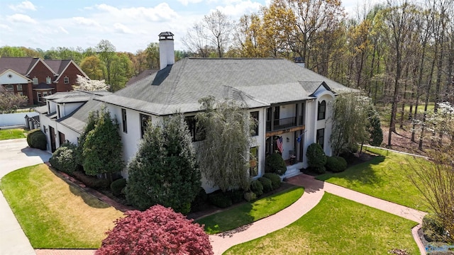 view of front of home featuring roof with shingles, a front lawn, a balcony, a chimney, and driveway