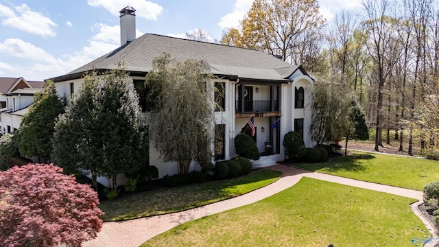 view of front of home featuring a front yard, a balcony, a chimney, and stucco siding