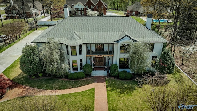 english style home with a shingled roof, a chimney, stucco siding, a front lawn, and a balcony