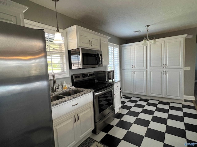 kitchen with stainless steel appliances, dark tile patterned floors, white cabinetry, sink, and pendant lighting