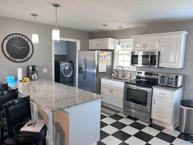 kitchen with appliances with stainless steel finishes, dark tile patterned floors, sink, washer / clothes dryer, and white cabinets