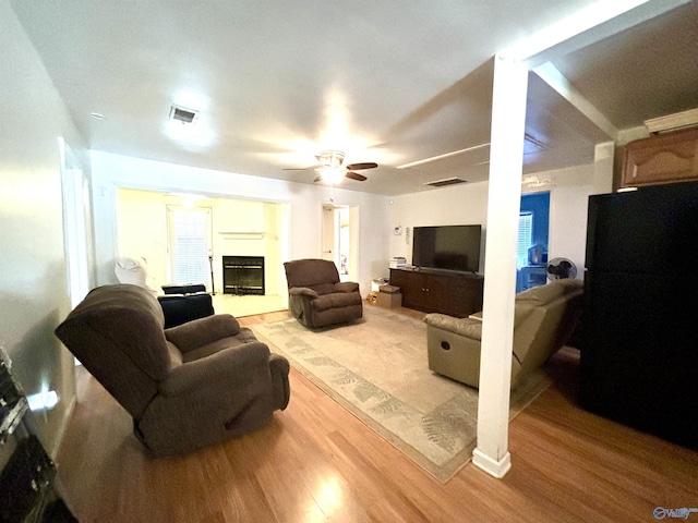 living area featuring ceiling fan, light wood-type flooring, a glass covered fireplace, and visible vents