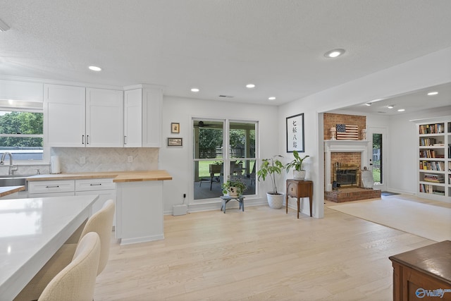 24961 Capshaw Rd, Athens, AL 35613 - kitchen featuring wood counters, light wood finished floors, white cabinetry, decorative backsplash, and a brick fireplace