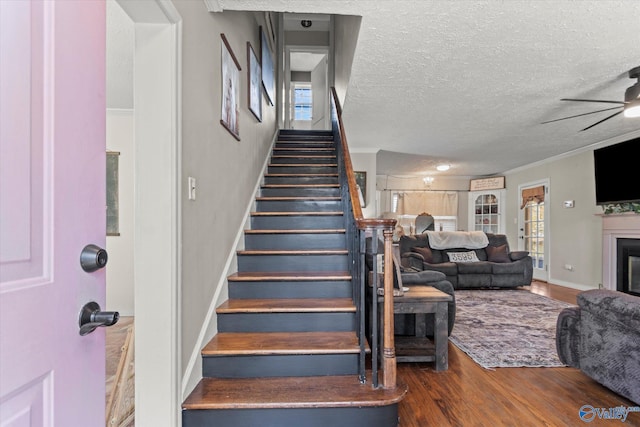 staircase with plenty of natural light, a textured ceiling, ceiling fan, a glass covered fireplace, and wood finished floors