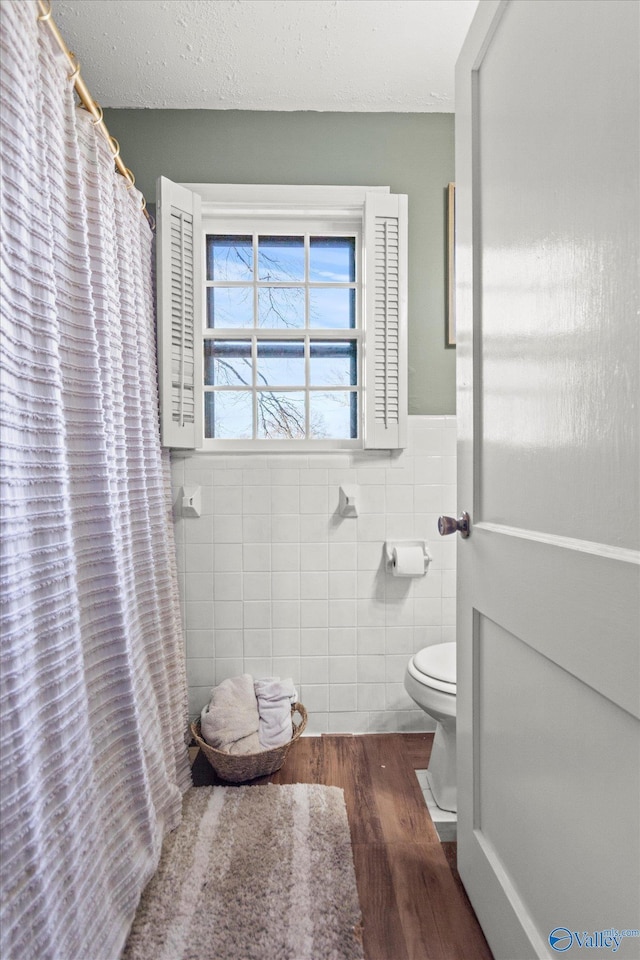 full bath with tile walls, a shower with shower curtain, wood finished floors, toilet, and wainscoting