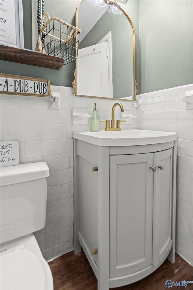 half bath with toilet, vanity, tile walls, and wainscoting