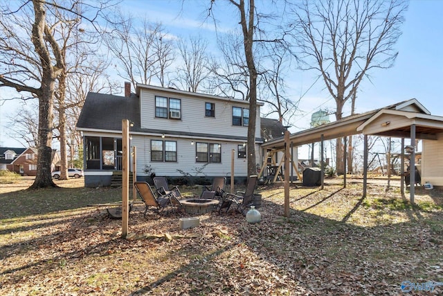 back of house featuring an outdoor fire pit, a chimney, a carport, and a sunroom