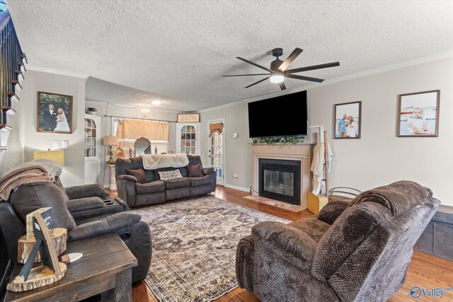 living room featuring a fireplace with flush hearth, crown molding, wood finished floors, and a ceiling fan